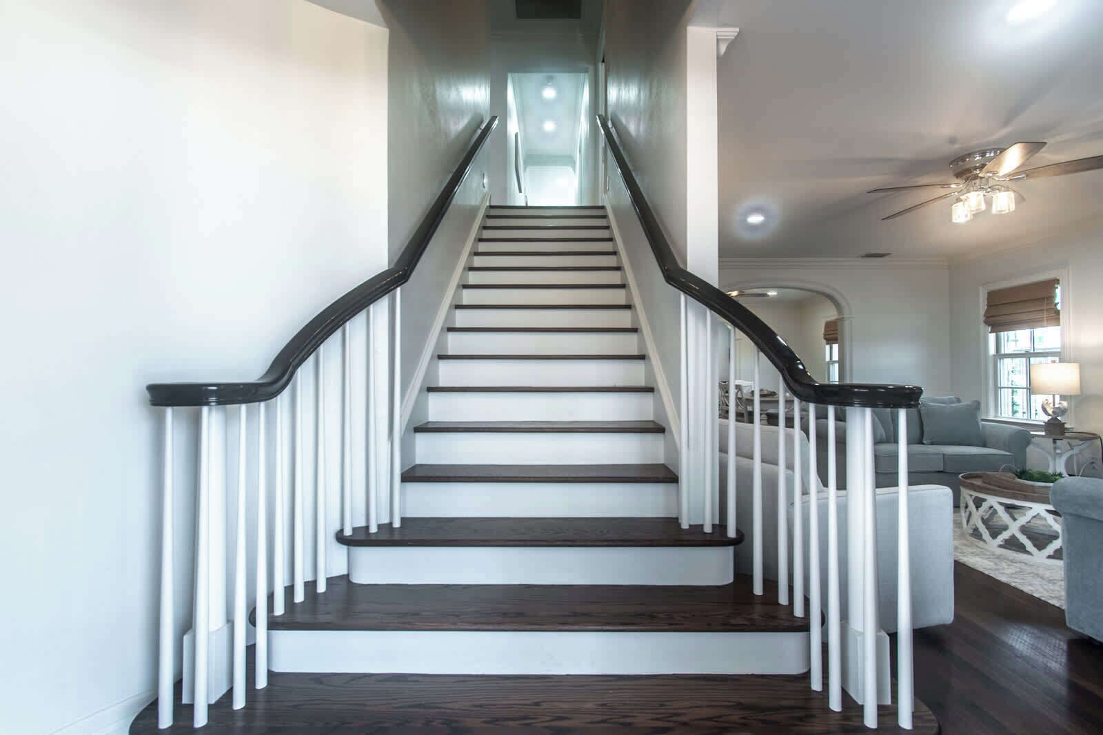 A staircase with white railings and dark steps, leading to a living area with a sofa and a lamp.