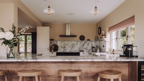 A kitchen with marble countertops, wooden stools, and a coffee machine. - Moss Ghyll | Hot Tub, Sauna & Cinema Room (Windermere)