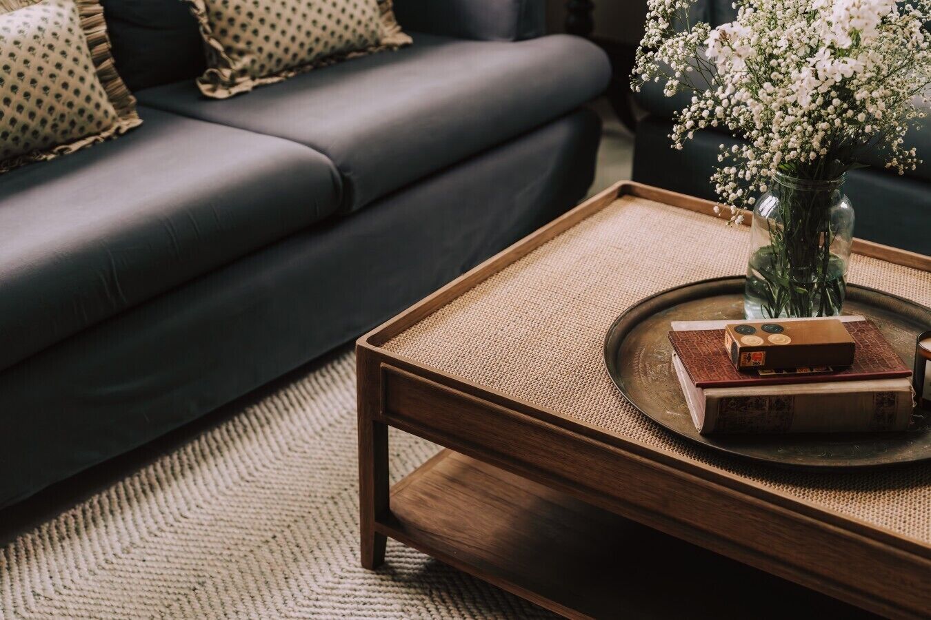 A dark leather sofa, a wooden coffee table with a woven top, and a vase with white flowers.