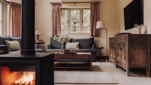A living room with a fireplace, a sofa, a coffee table, a TV, and a cabinet. - Moss Ghyll | Hot Tub, Sauna & Cinema Room (Windermere)
