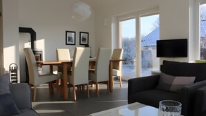 Ett modernt vardagsrum med en soffa, ett soffbord i glas, en matplats med stolar och bord, en öppen spis och en tv som är monterad på väggen.