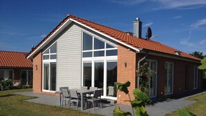 Ett tvåvåningshus med ett rött tegeltak, stora fönster och en uteplats med utemöbler.