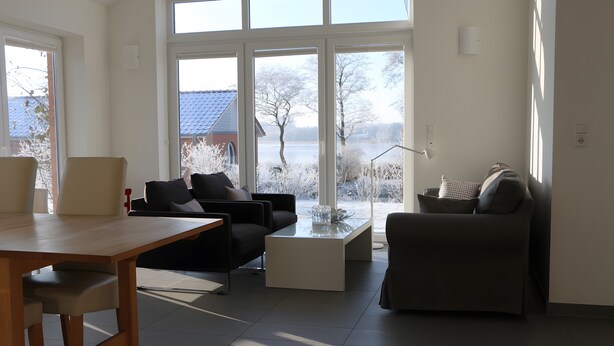 Ett modernt vardagsrum med ett matbord, två soffor och stora fönster med utsikt över ett hus och träd.