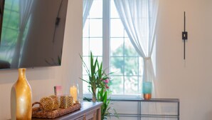 Een moderne woonkamer met een houten tv-meubel, een flatscreen televisie, een potplant en een raam met dunne gordijnen.