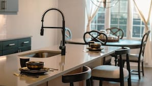 Een moderne keuken met een centraal eiland, barkrukken, hanglampen en een eethoek met stoelen.