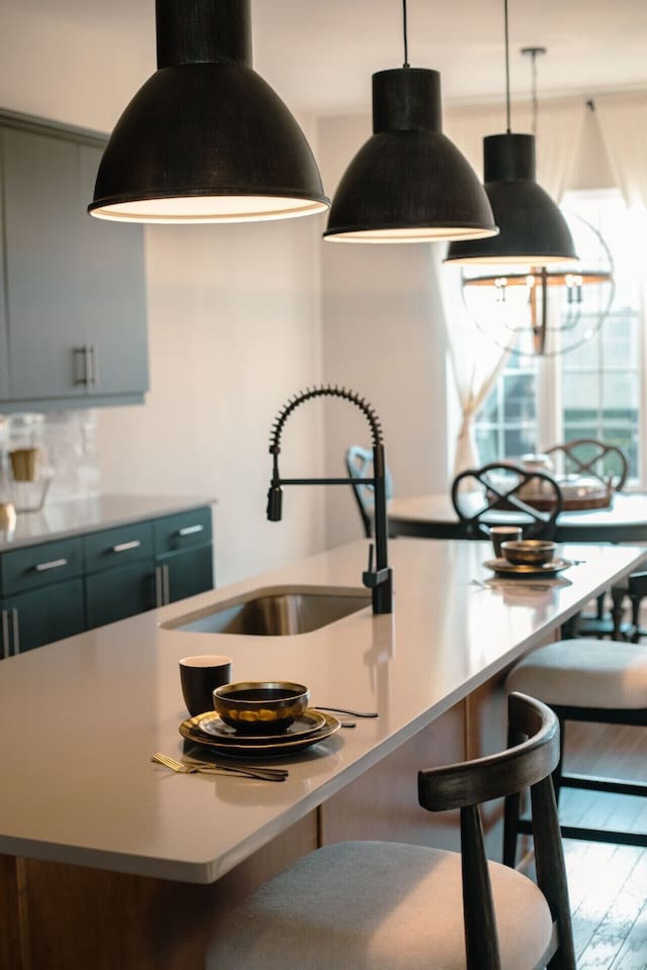 A modern kitchen with a central island, pendant lights, and a view of the dining area.
