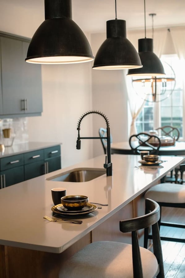 A modern kitchen with a central island, pendant lights, and a view of the dining area.