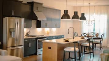 A modern kitchen with dark cabinets, stainless steel appliances, pendant lighting, and a central island with bar stools.