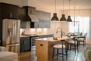A modern kitchen with dark cabinets, stainless steel appliances, pendant lighting, and a central island with bar stools.