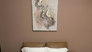 Een slaapkamer met een bed, twee kussens, een deken en een abstract schilderij aan de muur.