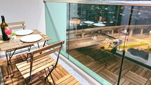 Un balcón con una mesa dispuesta para dos personas, una botella de vino y un vaso de agua.