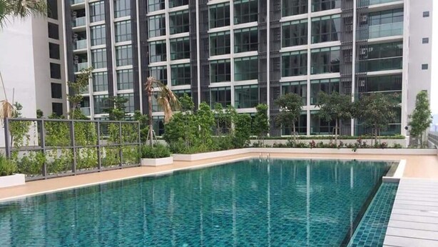 Piscina con bordes de azulejos, rodeada por una terraza de madera y una valla metálica.