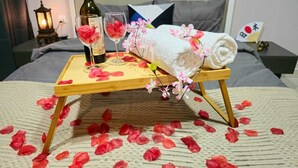 Una cama con una bandeja de madera que sostiene una botella, vasos y una toalla con flores.