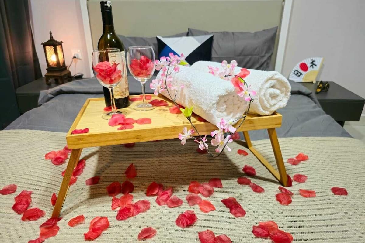 A bed with a wooden tray holding a bottle, glasses, and a towel with flowers.
