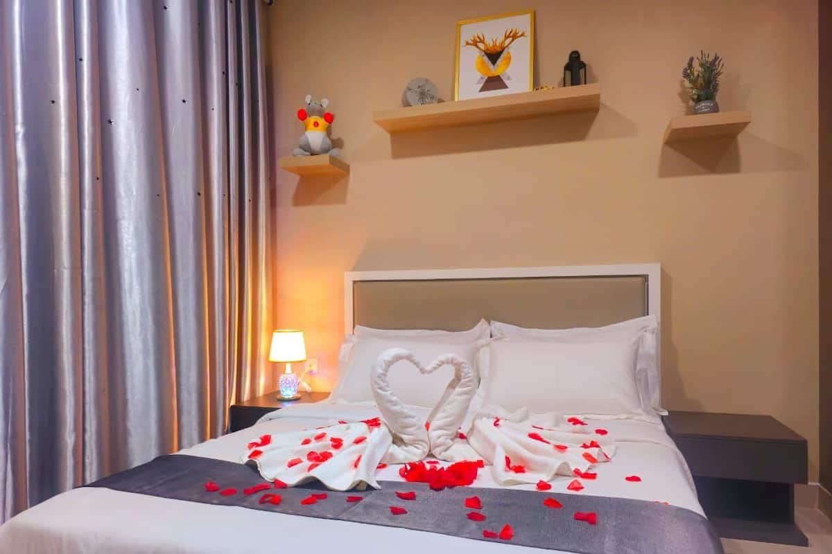 A hotel room with a bed, a nightstand, a lamp, and decorative items on shelves.