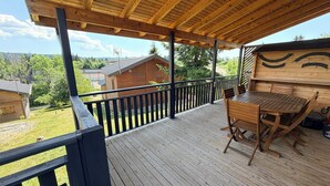 A wooden deck with a table and chairs, overlooking a forested area with houses. - Cozy chalet in the Haut-Jura with an indoor pool (Saint-Laurent-en-Grandvaux)