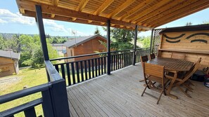 Una terraza de madera con mesa y sillas, con vistas a un área boscosa y casas.