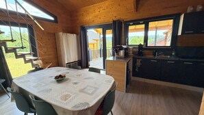 A wooden cabin with a dining table, chairs, a kitchen area, and a view of the outdoors. - Cozy chalet in the Haut-Jura with an indoor pool (Saint-Laurent-en-Grandvaux)