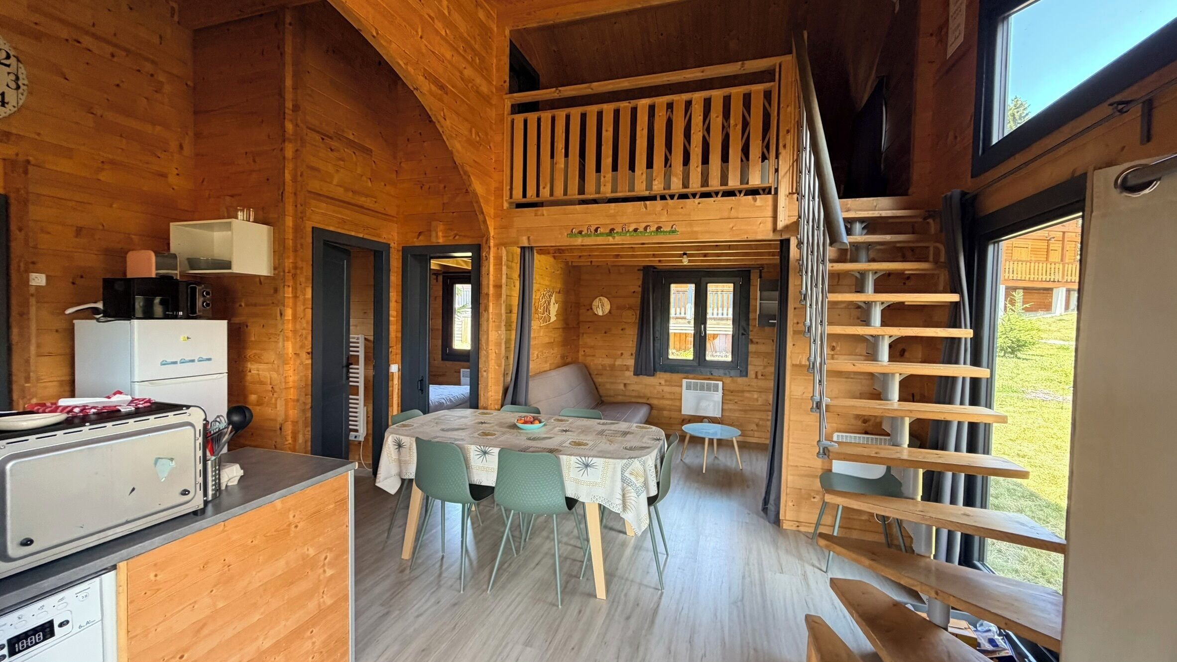 A wooden cabin interior with a kitchen, dining area, and a loft bedroom.