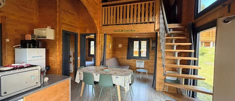 Interior de una cabaña de madera con cocina, comedor y un dormitorio en el altillo.