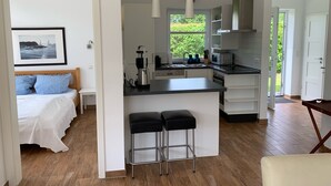 Une cuisine moderne avec un îlot central, un coin repas avec des tabourets de bar, une chambre avec vue et une porte donnant sur un jardin.