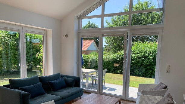 Un salon moderne avec un canapé, une table basse et des fauteuils en osier, de grandes fenêtres et une vue sur un jardin.