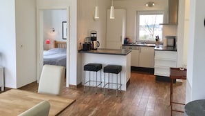 Une cuisine compacte équipée d’une machine à café, d’une bouilloire et d’un grille-pain. Elle comprend un coin repas avec une table et des chaises, ainsi qu’un petit tabouret de bar.