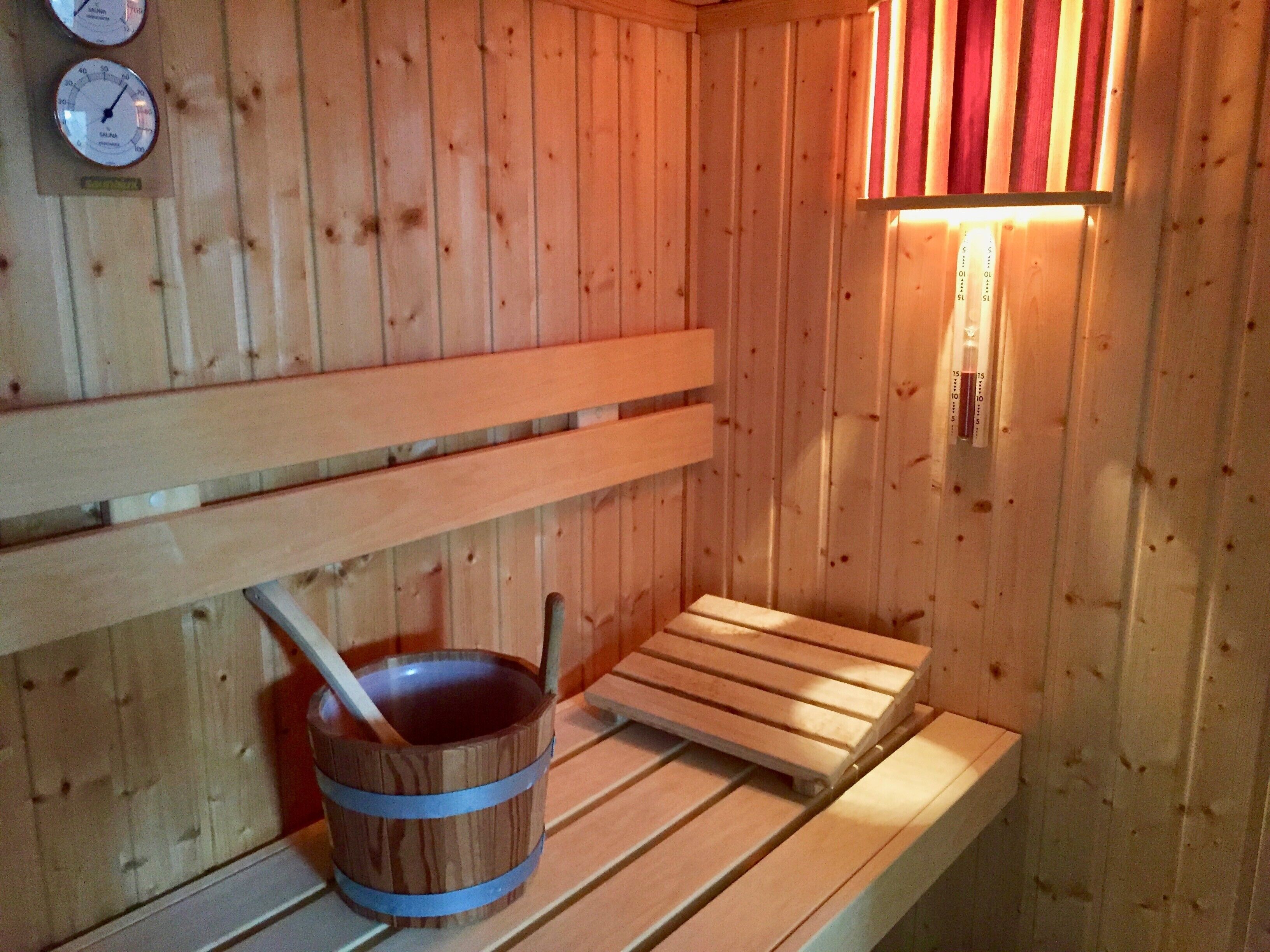 Un sauna en bois avec des bancs, un seau et un thermomètre accroché au mur.