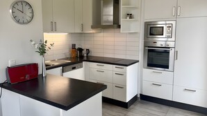 Moderni keittiö, jossa on valkoiset kaapit, musta työtaso, kello, kahvinkeitin ja mikroaaltouuni.