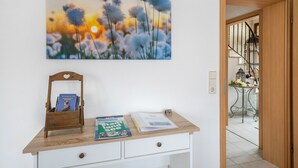 A room with a wooden desk, a framed painting of flowers, a small wooden chair, and a staircase leading to another area.