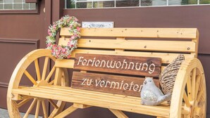 A wooden bench with a sign that reads 'Ferienwohnung zu vermieten' and a decorative wreath.