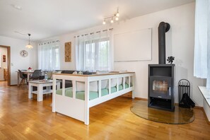 A modern living room with a sofa, a dining table, a white bench, a fireplace, and a kitchen area.