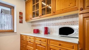A kitchen with wooden cabinets, a microwave, a red toaster, and a window with a curtain.