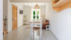 Una habitación con piso de madera, una mesa de comedor con sillas, un televisor montado en la pared y una puerta que da al exterior.