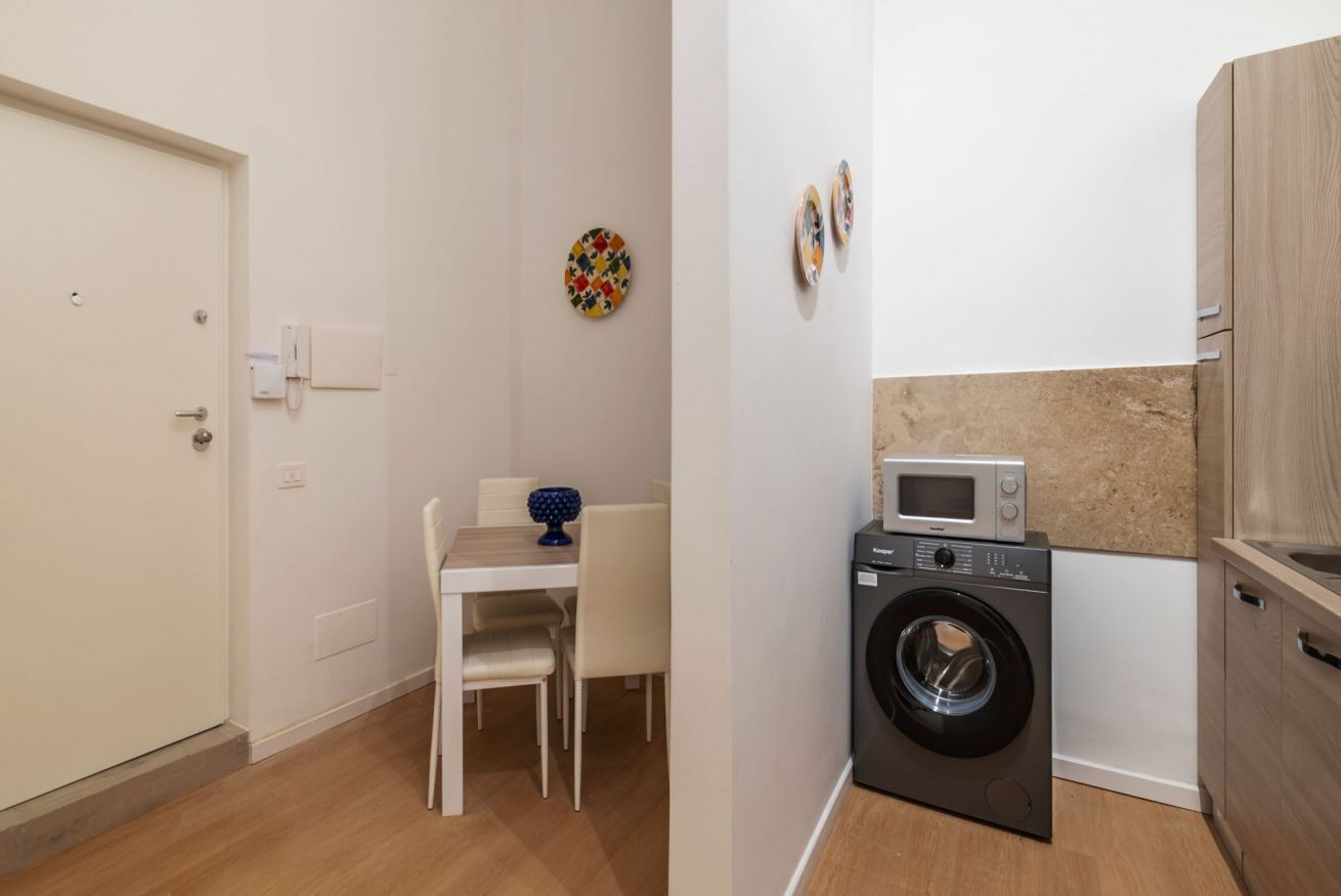 Une cuisine compacte équipée d’un lave-linge, d’un four à micro-ondes et d’un coin repas avec une table et des chaises.