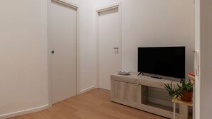 Una habitación con televisión sobre un mueble de madera, una puerta y una planta en maceta.