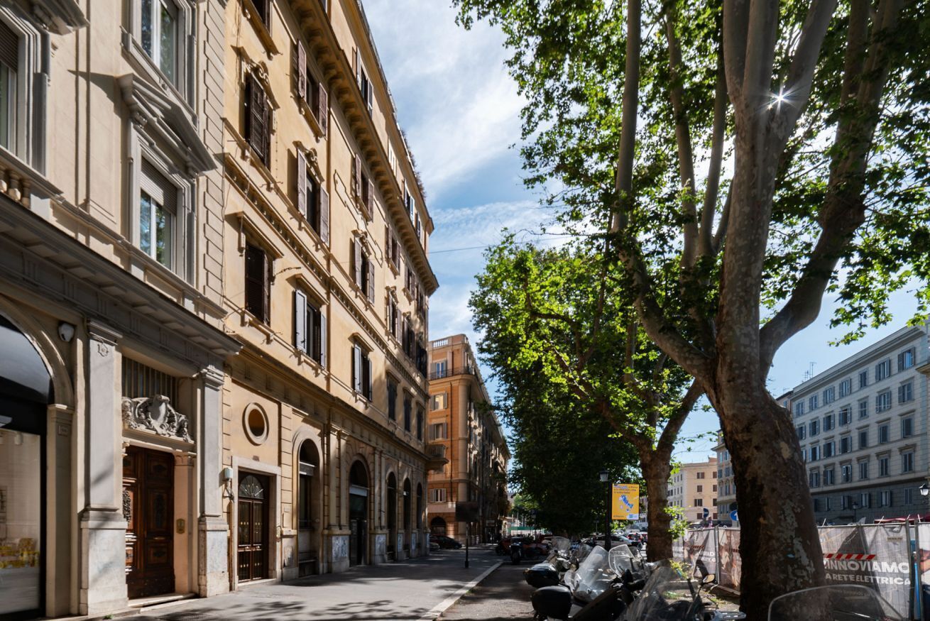 A street with historic buildings, a tree-lined sidewalk, and parked motorcycles.