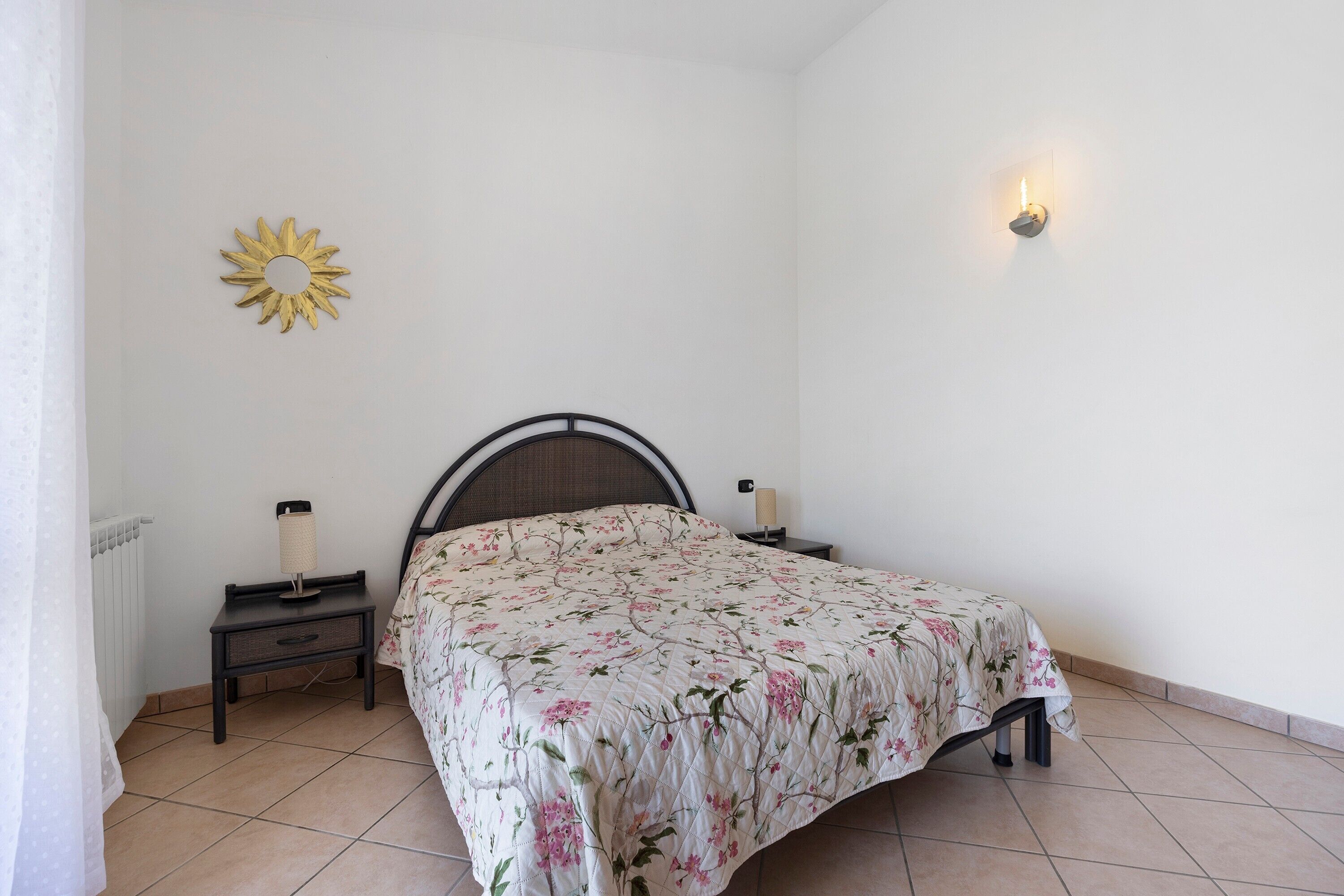 Una camera da letto con un letto, comodini, una lampada a parete e un elemento decorativo a forma di sole.