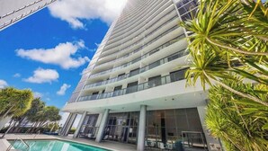 A modern hotel with a pool, palm trees, and a clear blue sky. - High-Rise One-Bedroom Condo In Edgewater Miami (Miami)
