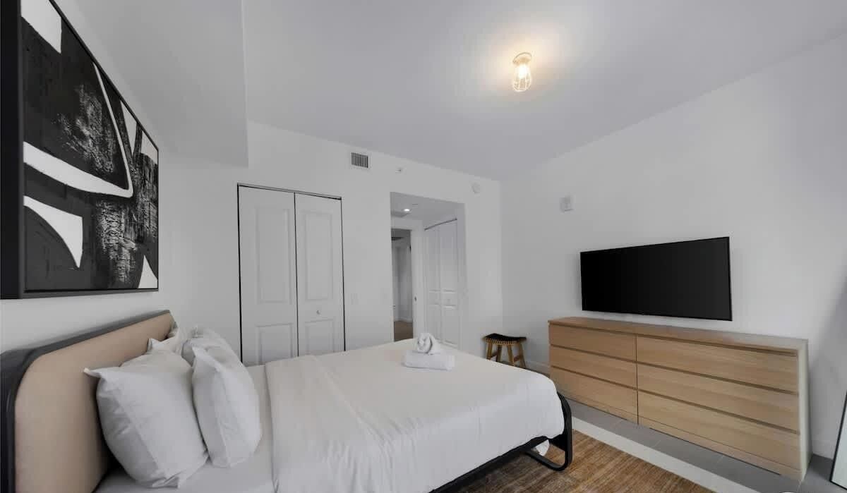 Een slaapkamer met een bed, een televisie, een kledingkast en een schilderij aan de muur.