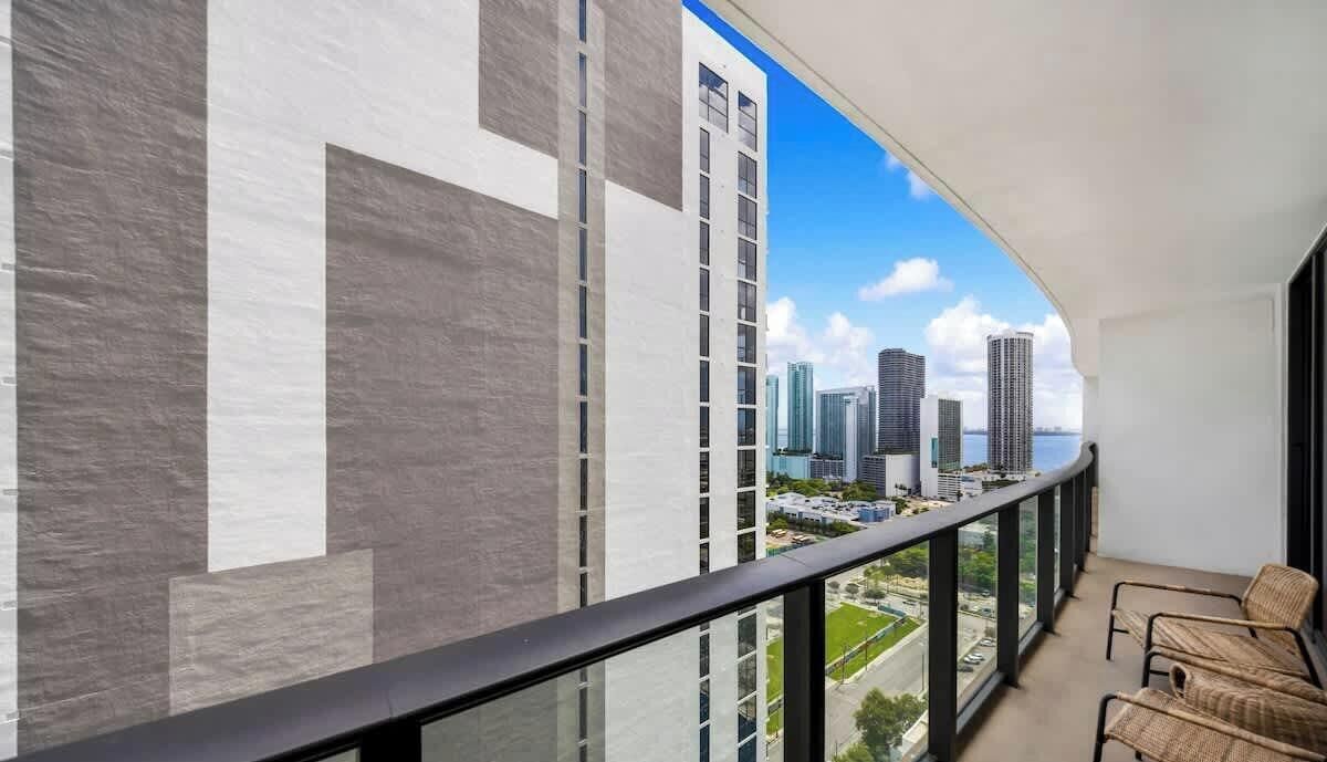 Een balkon met uitzicht op hoge gebouwen, een reling en rieten stoelen.