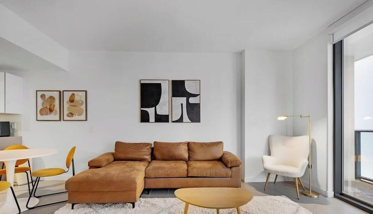 En moderne stue med en hjørnesofa, en hvid lænestol, et rundt sofabord og abstrakt kunst på væggen.