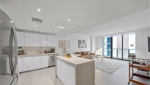 A modern kitchen with white cabinets, a central island, and a dining area with a sofa and table. - High-Rise One-Bedroom Condo In Edgewater Miami (Miami)