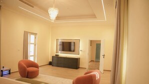 Ein modernes Schlafzimmer mit einem großen Bett, zwei Sesseln, einem Fernseher und einer Kommode.
