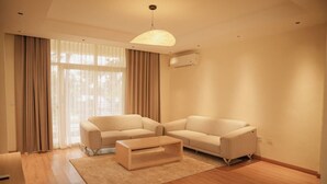 Ein modernes Wohnzimmer mit einer Sofagarnitur, einem Couchtisch und einem großen Fenster mit Vorhängen.