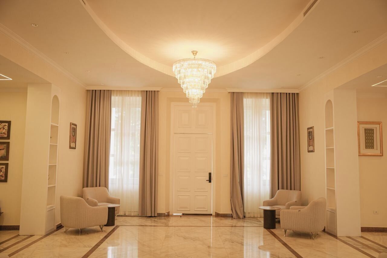 A spacious lobby with a grand chandelier, two armchairs, and a white door.