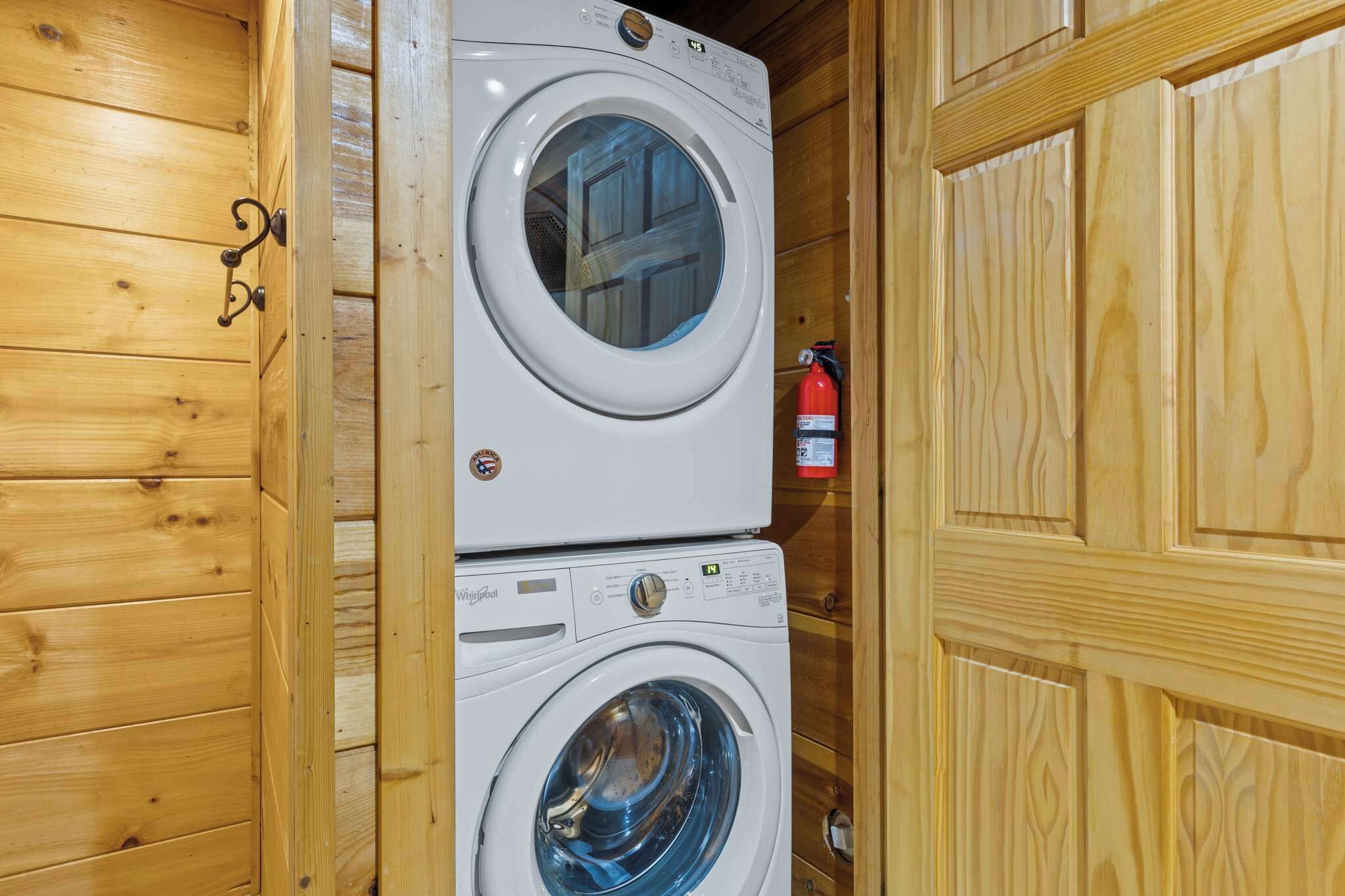 Une machine à laver et un sèche-linge superposés dans une pièce en bois, avec un extincteur fixé au mur.
