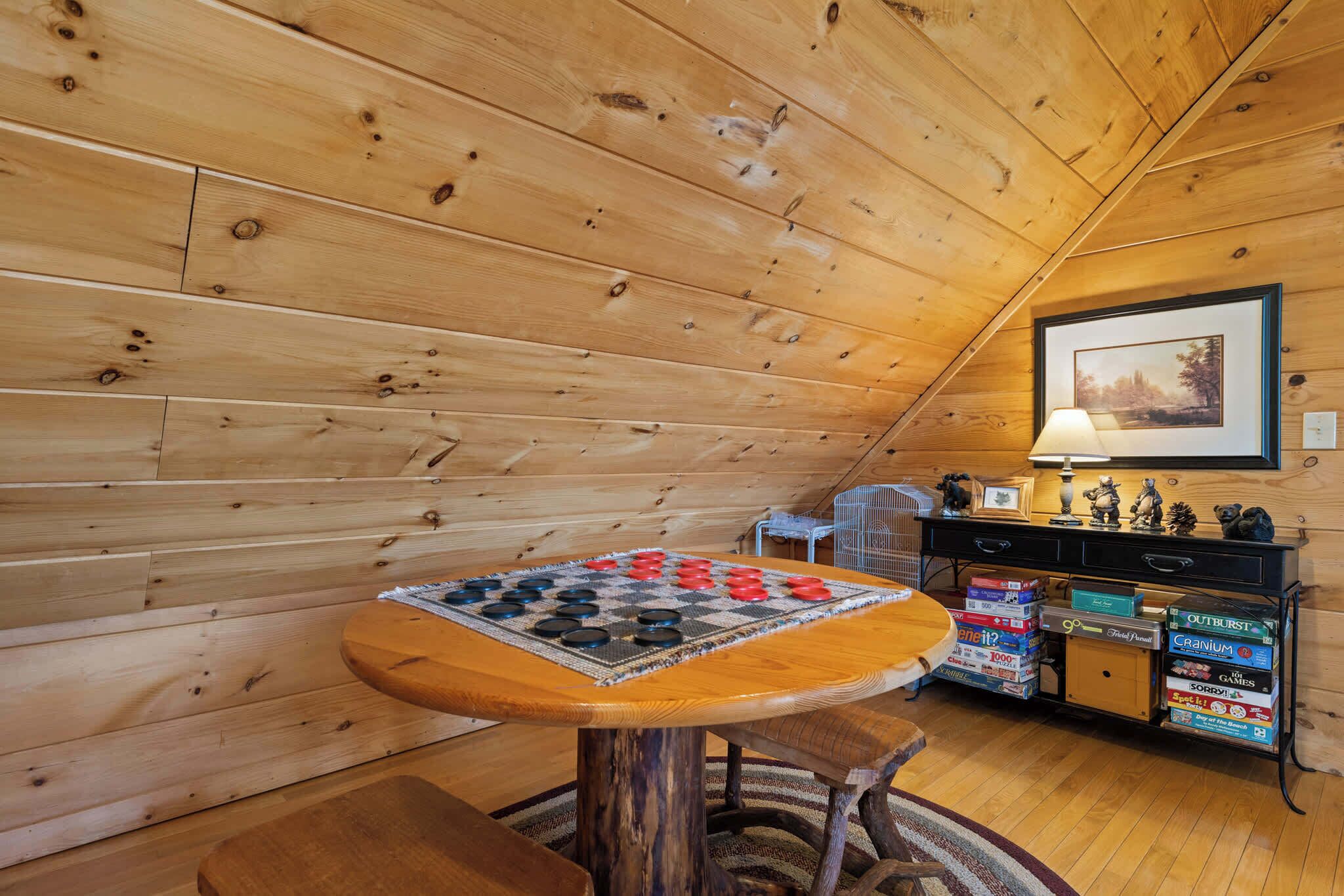 Ein Zimmer aus Holz mit einem Schachbrettspiel-Tisch, einem kleinen Stuhl, einer Lampe und einem Regal mit Aufbewahrungsboxen.