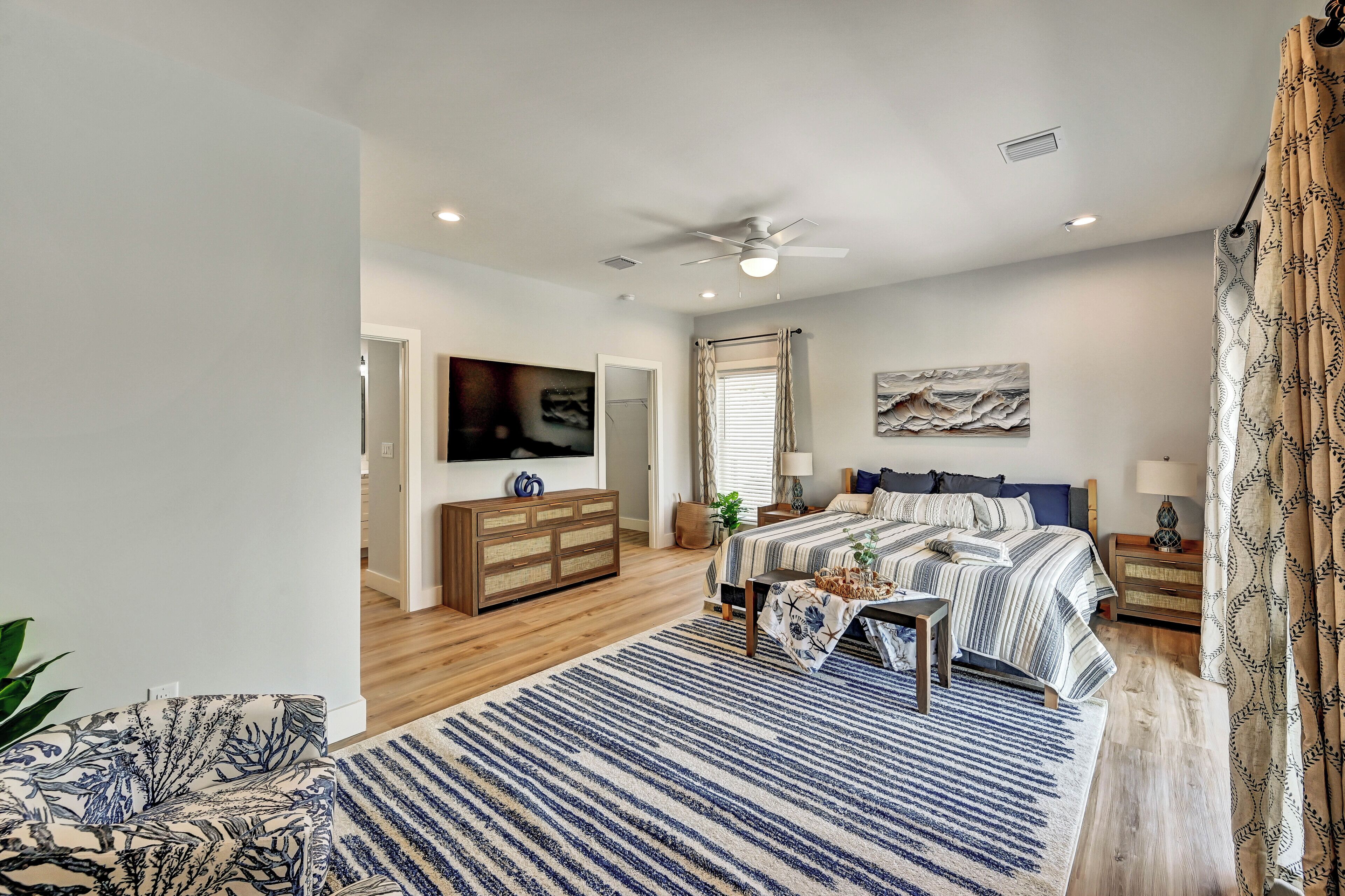 A bedroom with a bed, bedside tables, a ceiling fan, a TV, and a large window with curtains.