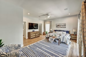 A bedroom with a bed, bedside tables, a ceiling fan, a TV, and a large window with curtains. - Pool Home Pet Friendly  Fenced Yard  Near Beach (Fort Myers)